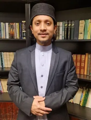 Nafies Dawah is standing in front of a bookshelf filled with religious texts